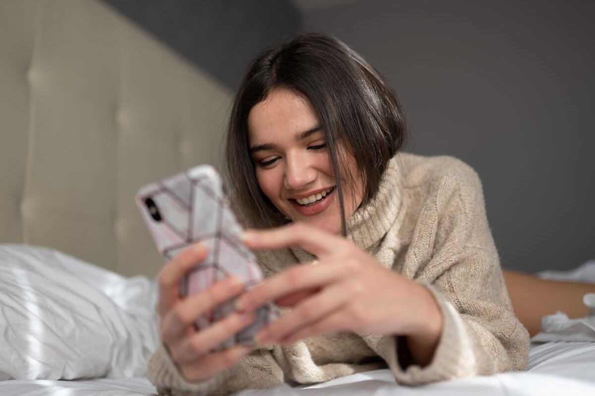 cheerful young lady messaging on bed